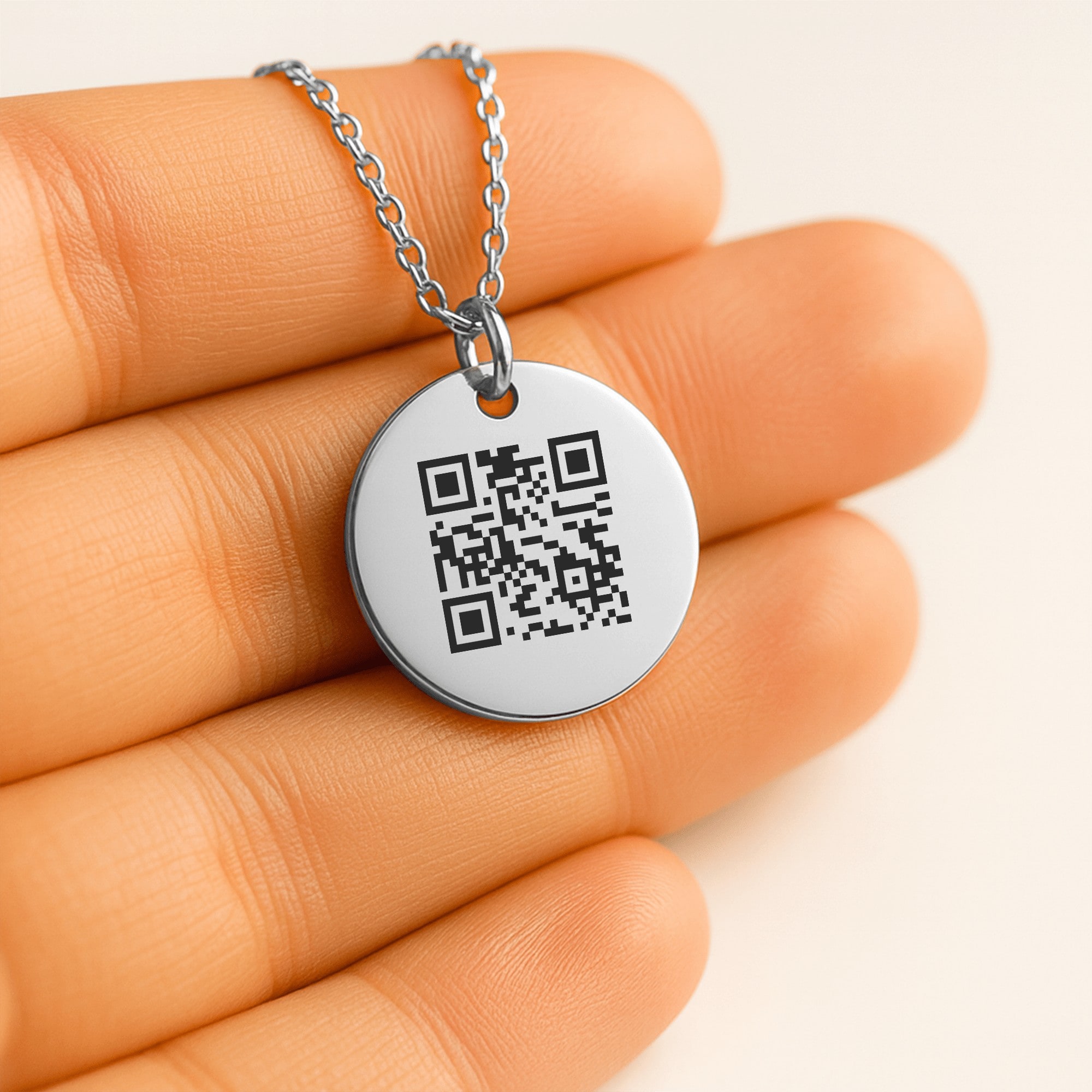 The coin pendant held in a hand, the engraved QR code filling the face.